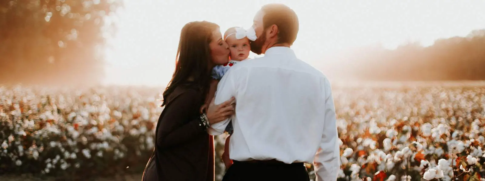 A man and woman kissing while holding their baby.